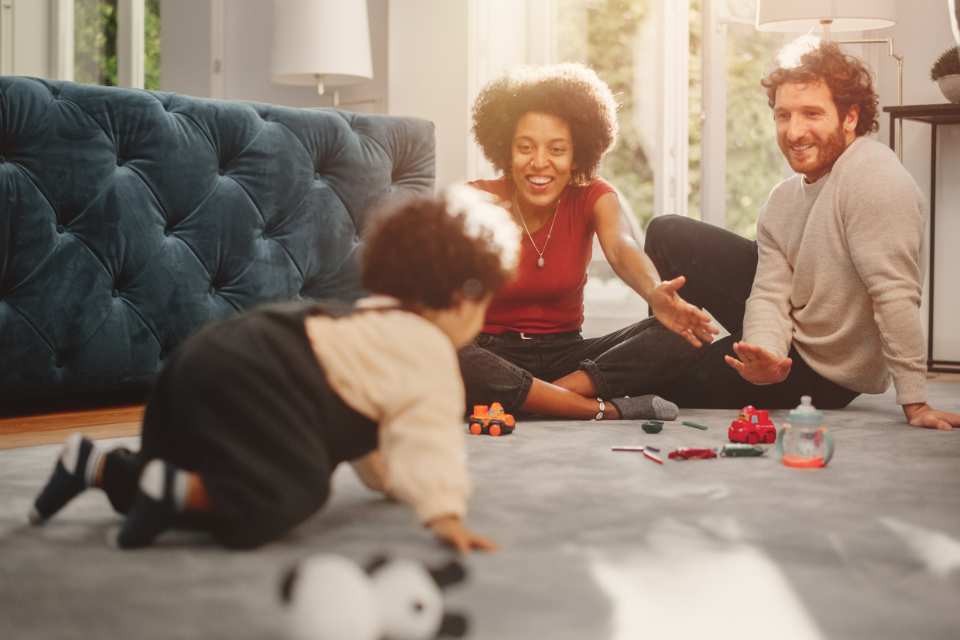 parents playing with child on plush grey carpet in modern living room with velvet blue couch